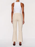 A model shown from the back wearing high-waisted cream-colored flared pants and a white sleeveless top, paired with dark brown shoes, against a plain light gray background.