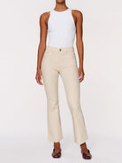 A model wearing a pair of light beige cropped flare jeans with a white sleeveless top and dark brown shoes, shown against a plain white studio background.