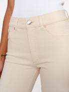 Close-up of a model wearing beige high-waisted denim jeans with a white ribbed top, showing the waistband, button, and front pockets.