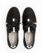 A pair of black slip-on sneakers with wide black laces tied in bows, white side stripes, and a white sole, shown from a top-down view on a white background. The insole displays the brand name 'Gabor'.