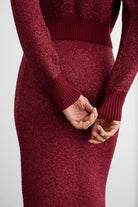 A close-up of a person wearing a sparkling burgundy knit sweater and matching skirt, showing the ribbed cuffs and waistband against a light gray background.
