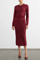 A model wearing a burgundy knit cardigan and matching midi skirt set, paired with matching burgundy heels, against a plain light gray studio background.