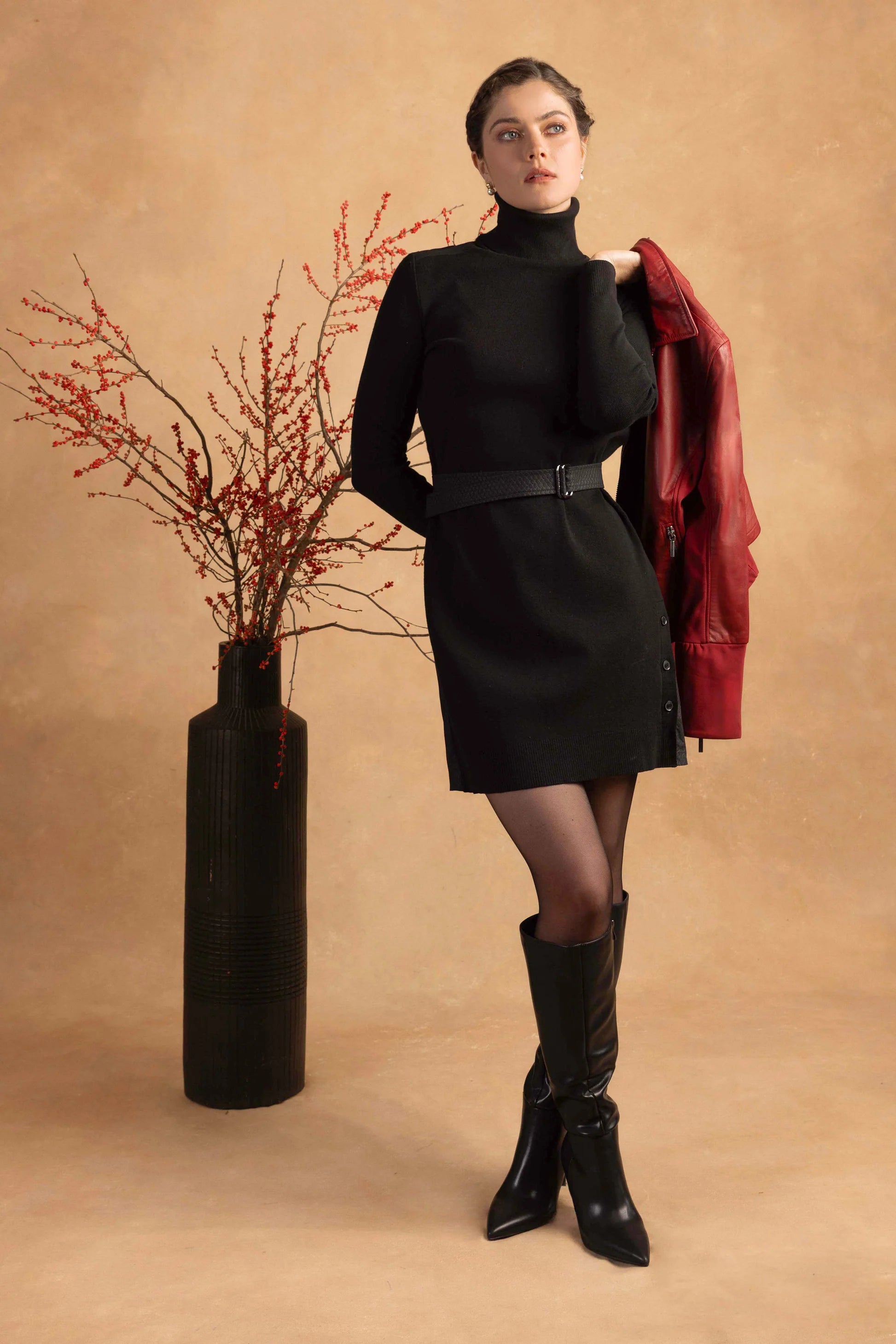 Woman in black outfit with red jacket against a beige background