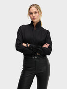 Person wearing a black outfit with a high collar on a light gray background